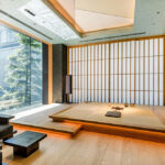 Modern Japanese-style room with a raised tatami platform, shoji screens, and a large window overlooking a garden.