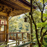 Traditional Japanese shrine with intricate wooden carvings, set amidst lush forest trees in vibrant green and golden hues.