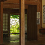Interior of a traditional Japanese wooden house with tatami floors, shoji doors, and calligraphy scrolls on the wall.