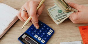 A person using a calculator while holding cash, with a notebook and receipts on the table