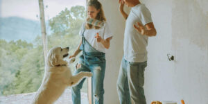 A couple dances with a golden retriever in a partially renovated room with an open doorway overlooking greenery