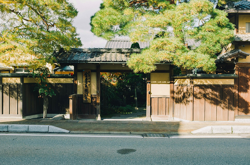 A small Japanese house with a gate stands in front of a tree, creating a serene and inviting atmosphere