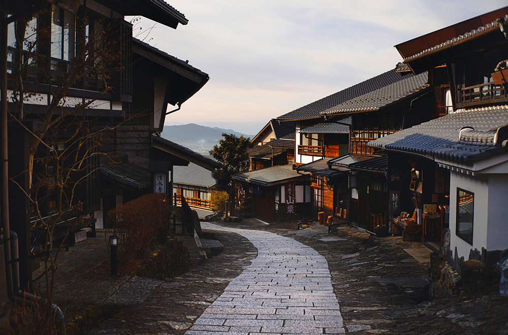 A narrow cobblestone street in Japan, lined with traditional buildings and vibrant greenery, inviting exploration and discovery