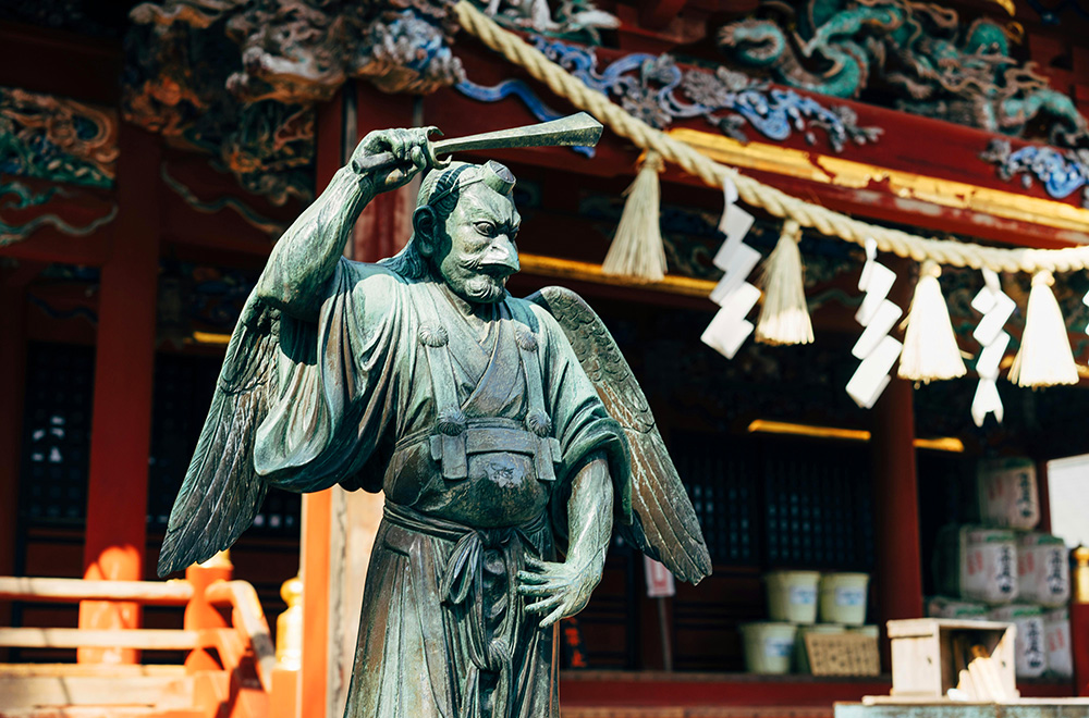 A statue of an Asian man holding a sword, representing a Tengu, located in a temple setting in Japan