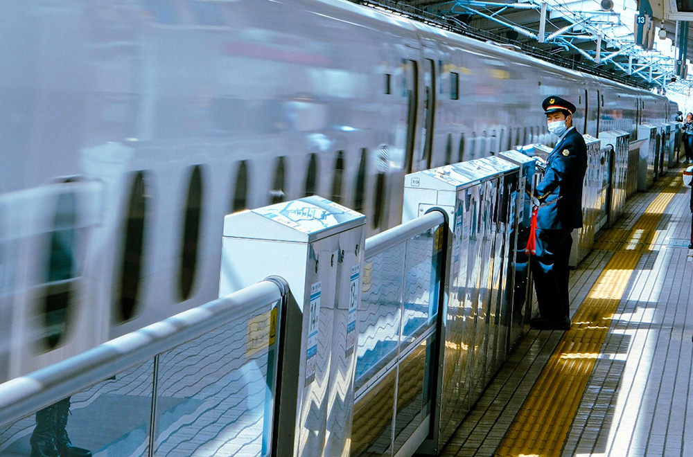 A man in a blue uniform stands beside a train in Japan, showcasing the country's railway culture and professionalism