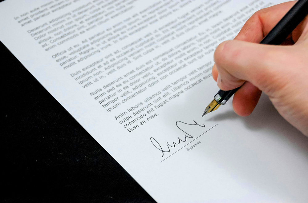 A person signing a contract with a pen, symbolizing the formal agreement and commitment to the terms outlined