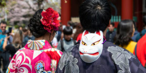 Couple in traditional Japanese attire at a festival, with a kitsune mask and floral hair accessory.
