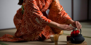 A woman in a kimono gracefully pours tea into a pot during a traditional Japanese tea ceremony