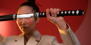Woman holding a katana horizontally in front of her face with a focused expression.