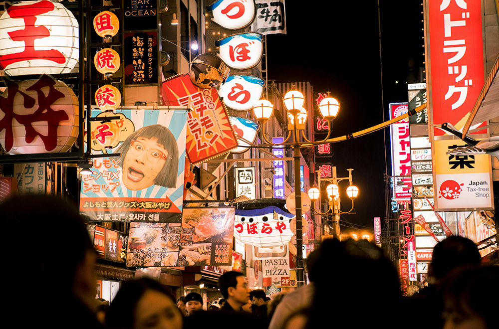 A bustling night street in Japan, filled with numerous pedestrians navigating the vibrant urban landscape.
