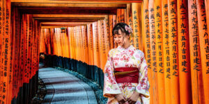 A young woman in a floral kimono stands gracefully among the vibrant red torii gates of Fushimi Inari Shrine in Kyoto, Japan.