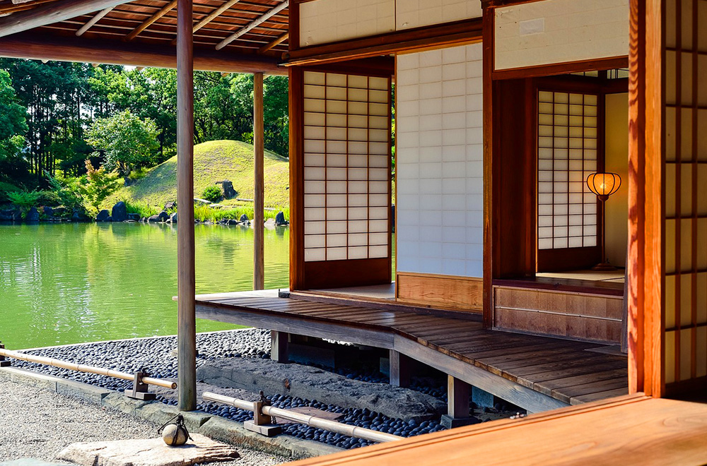 Traditional Japanese tea house with shoji sliding doors, overlooking a serene pond and lush green garden.