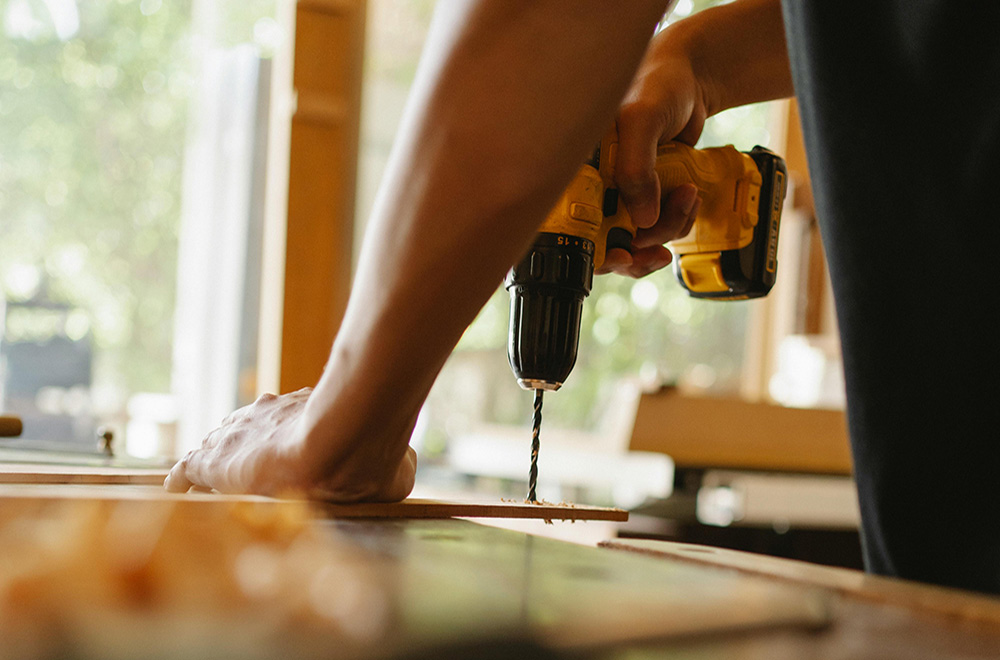 Close-up of a person using a power drill while working on wood indoors.