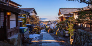 Traditional Japanese village street with wooden houses and a mountain view in the distance.