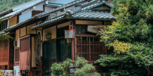 Classic Japanese wooden house surrounded by greenery in a quiet countryside setting.