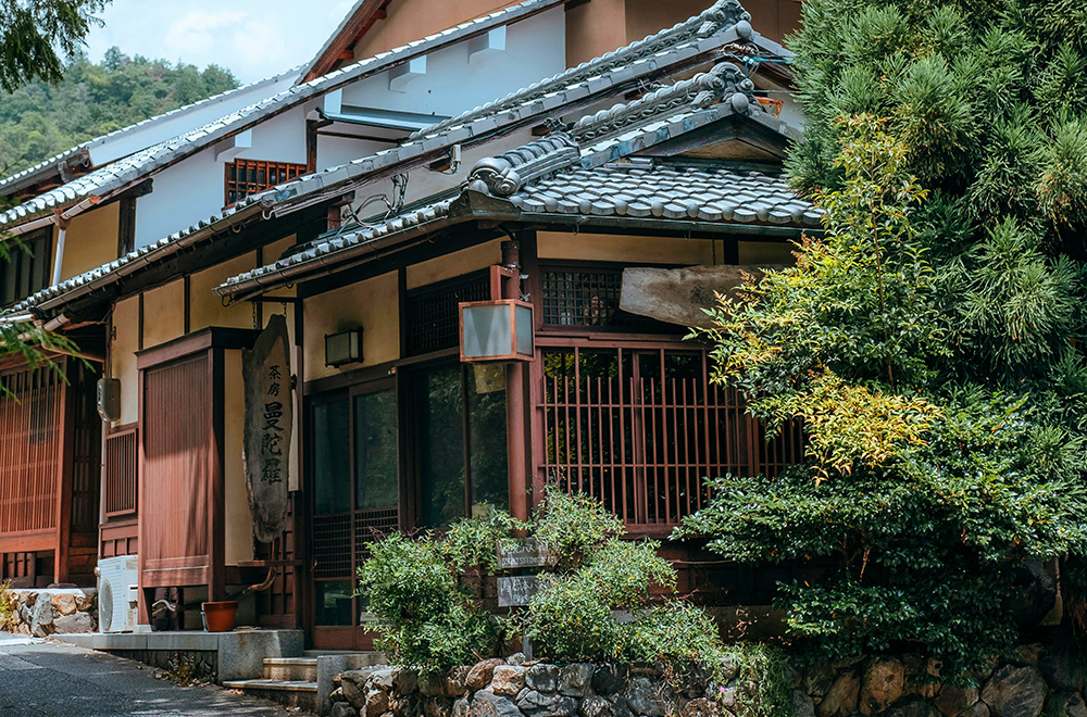 Classic Japanese wooden house surrounded by greenery in a quiet countryside setting.