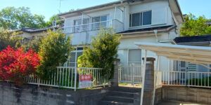 Spacious two-story Japanese house with a front garden, white exterior, gated entry, and covered carport in a sunny suburban area.