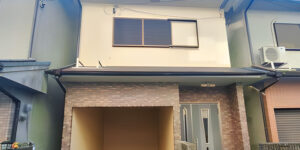Two-story urban Japanese house with a built-in carport and modern facade, located between adjacent buildings.