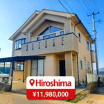 Two-story house with a modern roof and large windows, featuring a driveway and parking space, listed for sale in Japan.