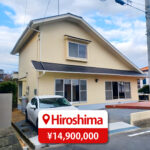 Two-story house with a modern roof and large windows, featuring a driveway and parking space, listed for sale in Japan.
