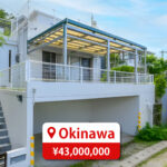 Two-story house with a modern roof and large windows, featuring a driveway and parking space, listed for sale in Japan.