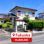 Two-story house with a modern roof and large windows, featuring a driveway and parking space, listed for sale in Japan.