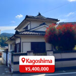 Two-story house with a modern roof and large windows, featuring a driveway and parking space, listed for sale in Japan.