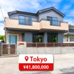 Two-story house with a modern roof and large windows, featuring a driveway and parking space, listed for sale in Japan.
