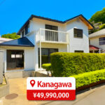 Two-story house with a modern roof and large windows, featuring a driveway and parking space, listed for sale in Japan.