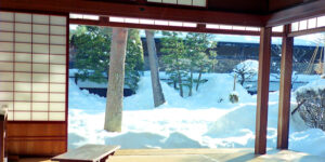 Traditional Japanese tatami room with shoji screens opening onto a snow-covered garden with trees in winter.
