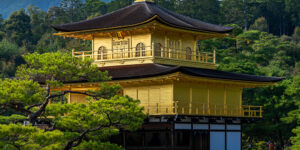 Kinkaku-ji, the Golden Pavilion in Kyoto, a gold-leaf-covered Zen temple surrounded by green trees and forested hills.