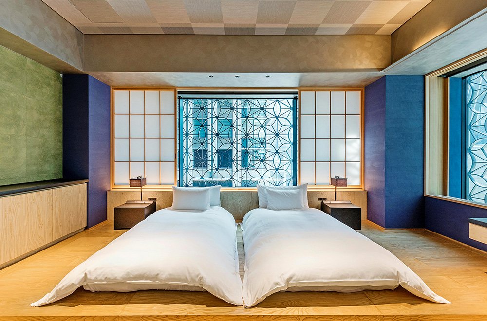 Modern Japanese-style bedroom with two low beds, white bedding, wooden floors, shoji-style panels, and a decorative patterned window.