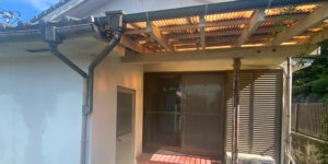 Exterior view of a traditional Japanese house with a tiled roof, wooden-framed sliding window, small awning with translucent panels, and an outdoor air conditioning unit mounted on the wall.